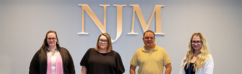 Group shot in NJM lobby of employees Amanda, Rachelle, Mike, and Missy in front of NJM sign.