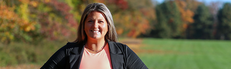 Photo of NJM employee, Amanda, with fall scenery in the background.