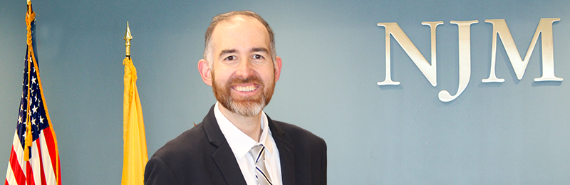 NJM employee Kevin in front of NJM sign and flags.