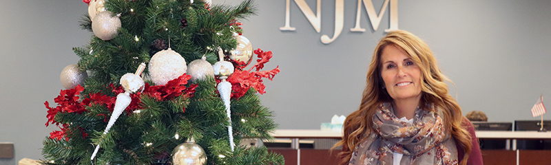 Headshot of NJM employee, Melissa, in NJM lobby next to holiday tree.