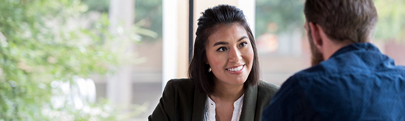 Cheerful Hispanic businesswoman smiles while meeting with client.